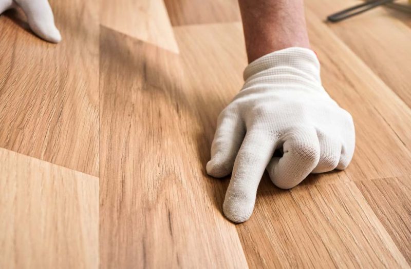 Close-up of a worker’s hand adjusting a light wood plank in place, ensuring every piece fits perfectly during the flooring installation process.