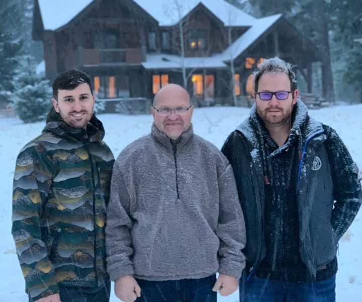 Three men standing in front of a large house during winter, showcasing teamwork and the home's cozy, welcoming exterior.