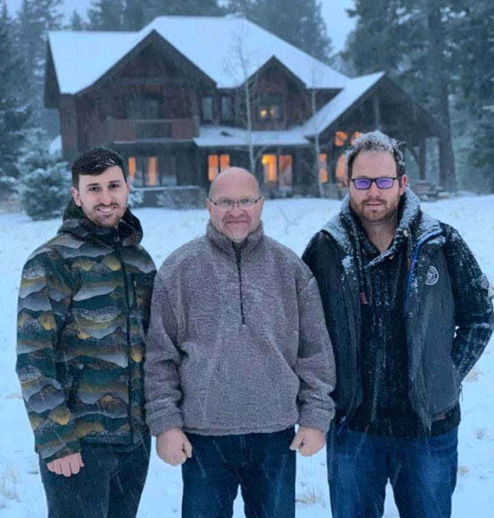 Three men standing in front of a large house during winter, showcasing teamwork and the home's cozy, welcoming exterior.
